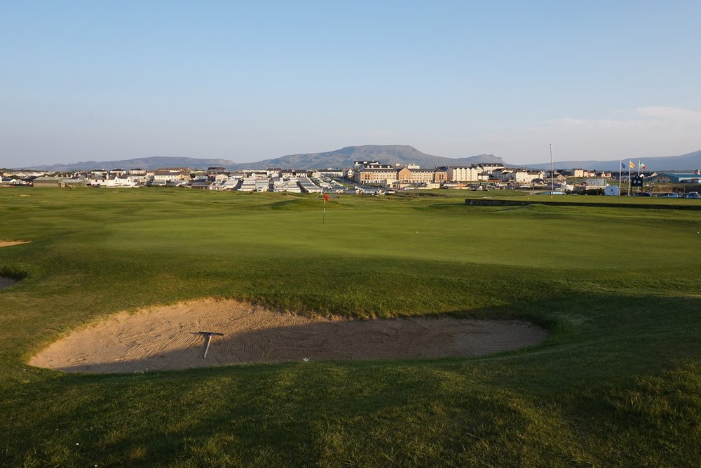 A links green with a flag and a deep bunker in low evening sun